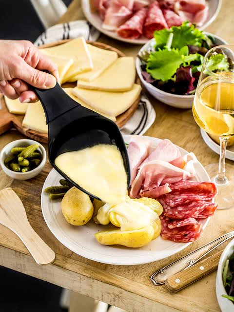 Ilustración de media rueda de queso raclette fundiéndose junto al fuego frente a los Alpes del Valais