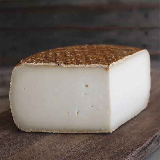Ilustración de una rueda de tomme de chèvre de corteza gris frente a los Pirineos con cabras